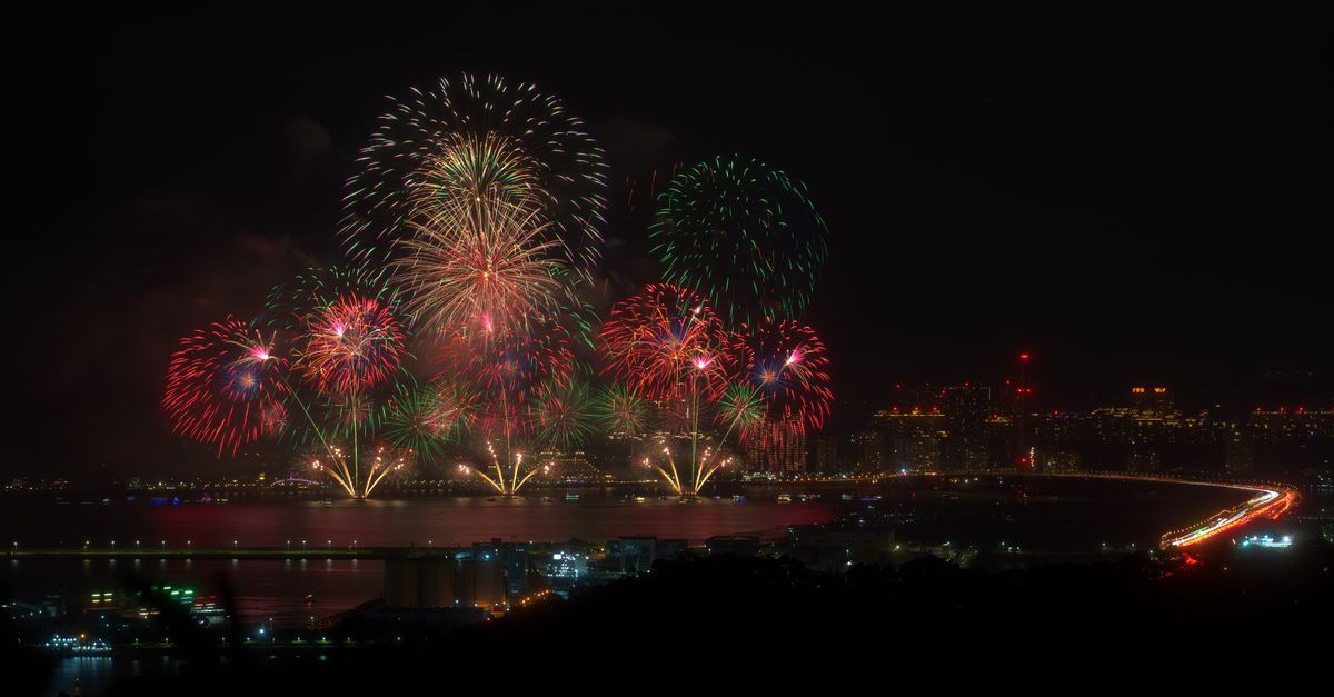 Fireworks display over a city skyline reflecting on water at night