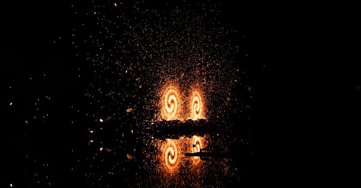 Synchronized fireworks display reflecting on calm water during a choreographed pyromusical show